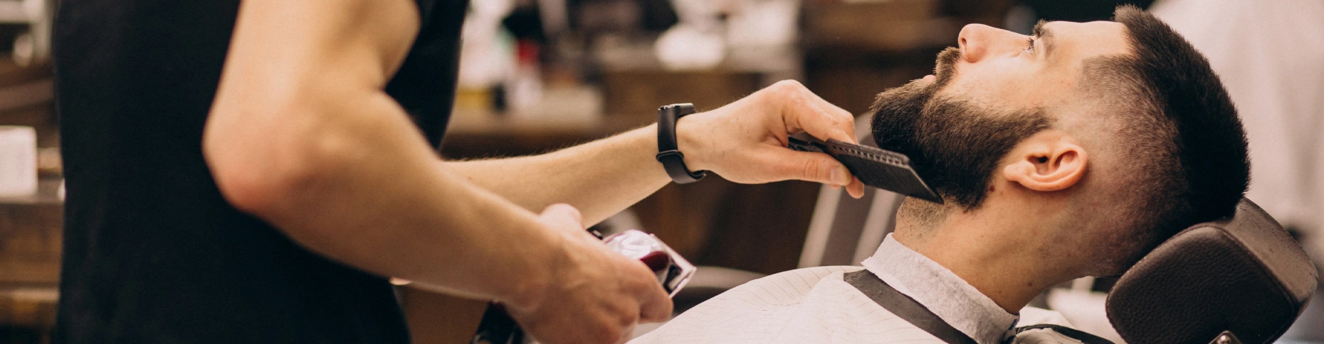 Barbeiro profissional a aparar a barba de cliente na barbearia, prática para curso de barbeiro