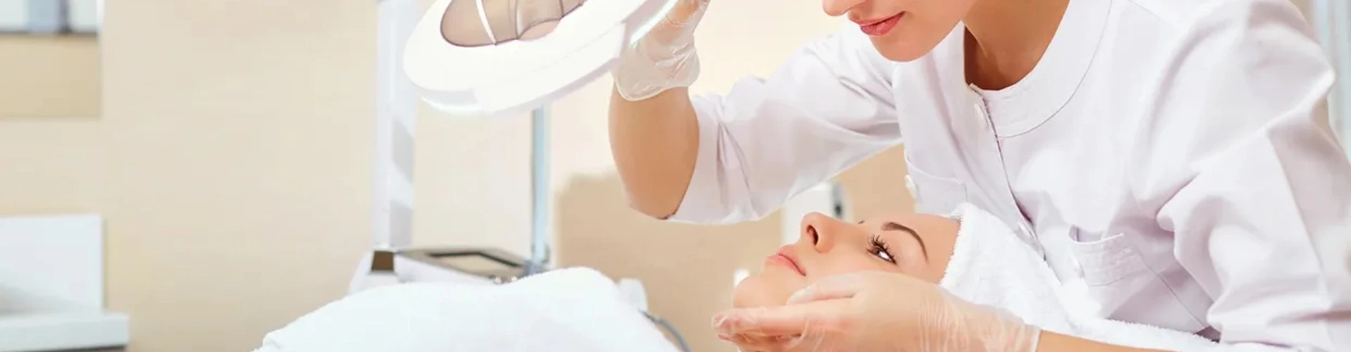 Esteticista a examinar a pele de uma cliente com lupa e luz de aumento durante tratamento facial profissional